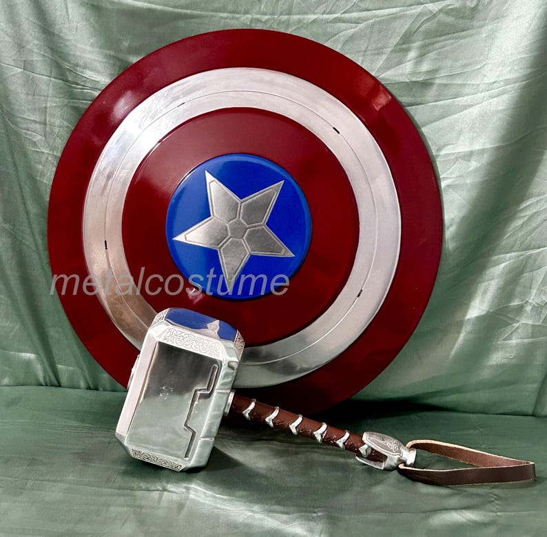 Op de afbeelding: Een rood, wit en blauw Captain America schild met een zilveren ster in het midden. Een zilveren en zwarte Thor's hamer met een bruine leren riem is op de voorgrond.