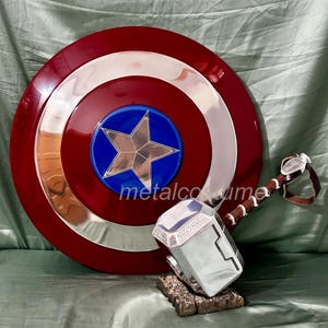 Op de afbeelding: Een rood, wit en blauw Captain America-schild met een zilveren ster in het midden, en een zilveren Thor-hamer met een bruine leren handgreep.
