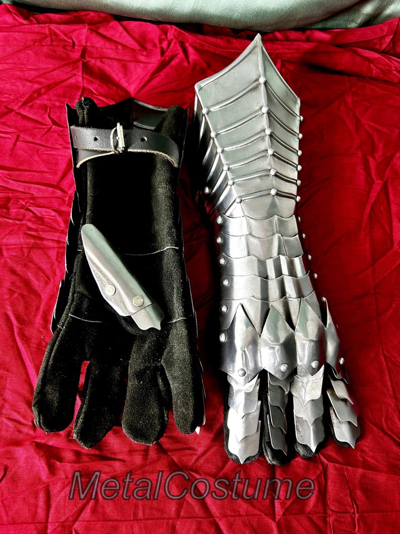 May include: A pair of medieval-style gauntlets, one made of black leather and the other of metal with a scaly design. The metal gauntlet has a pointed fingertip design.