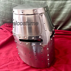 May include: A silver medieval helmet with a visor and rivets. The helmet is made of metal and has a textured surface.
