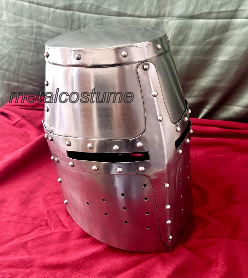 May include: A silver medieval helmet with a visor and rivets. The helmet is made of metal and has a textured surface.