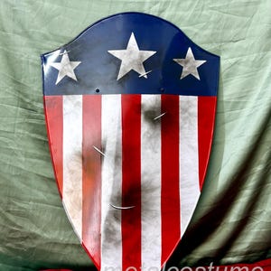 Puede incluir: Un escudo rojo, blanco y azul con un aspecto desgastado. El escudo tiene cinco estrellas blancas sobre un fondo azul y rayas rojas y blancas.
