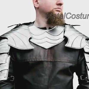 Könnte beinhalten: Silberne Schulterpanzerung aus Metall mit geschichteten Platten und dekorativen Kanten. Die Rüstung wird über einer dunkelbraunen Lederjacke getragen. Der Text "MetalCostume" ist in der oberen rechten Ecke sichtbar.