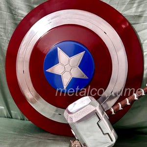 Op de afbeelding: Een rood, wit en blauw Captain America schild met een zilveren ster in het midden, en een zilveren Thor's hamer met een bruine handvat.