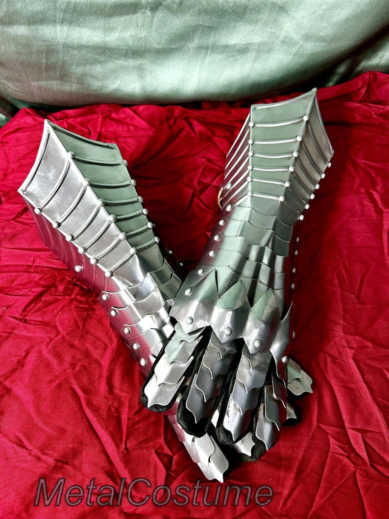 May include: A pair of silver metal gauntlets with a scaly design. The gauntlets are made of interlocking metal plates and have a pointed fingertip design.