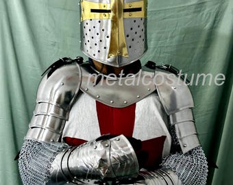 May include: A full suit of medieval armor, including a helmet with a gold cross, shoulder guards, and arm protection. The chest piece features a red cross on a white background. The text "metalcostume" is visible on the chest.