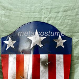 Puede incluir: Un escudo rojo, blanco y azul con tres estrellas blancas. El escudo est&aacute; hecho de metal y tiene un aspecto desgastado. El texto "metalcostume" es visible en el escudo.