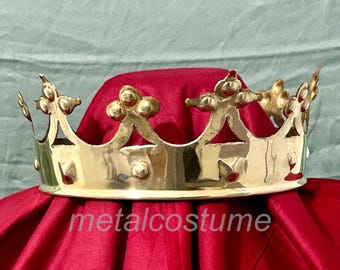 Könnte beinhalten: Eine goldene Metallkrone mit einer spitzen Spitze und dekorativen Details. Die Krone liegt auf einem roten Samttuch.