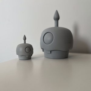 May include: Two gray ceramic figurines with a rounded shape and a pointed top. The larger figurine is about twice the size of the smaller figurine.