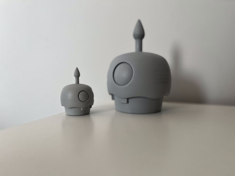 May include: Two gray ceramic figurines with a rounded shape and a pointed top. The larger figurine is about twice the size of the smaller figurine.