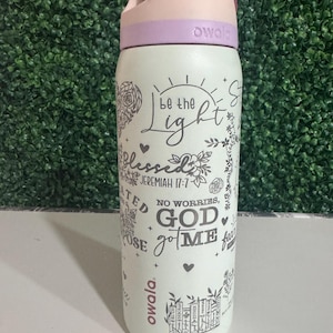 May include: A white Owala water bottle with a light purple lid and handle. The bottle features the text "be the Light" and "No worries, God got me" with floral and heart designs. The bottle is approximately 10 inches tall.