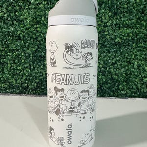 May include: White insulated water bottle with a gray lid and a flip-top spout. The bottle features black and white illustrations of Peanuts characters, including Charlie Brown and Snoopy. The word "PEANUTS" is printed on the bottle.