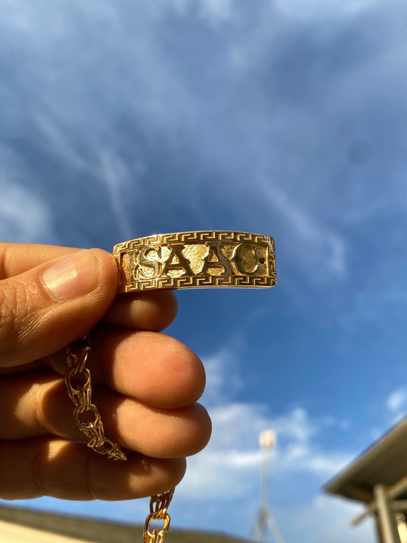 May include: A gold chain necklace with a pendant that says "VERSACE" in a Greek key design.