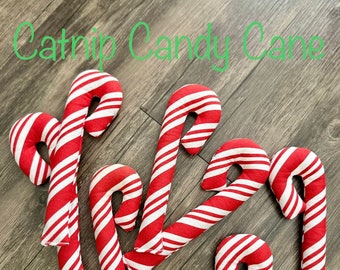 May include: A collection of red and white striped catnip candy canes, arranged on a wooden surface. The text "Catnip Candy Cane" is written in green cursive script above the candy canes.