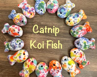 May include: A circle of 15 colorful catnip koi fish toys. The toys are made of soft, fuzzy fabric with a white base and colorful spots. The text "Catnip Koi Fish" is written in yellow letters in the center of the circle.