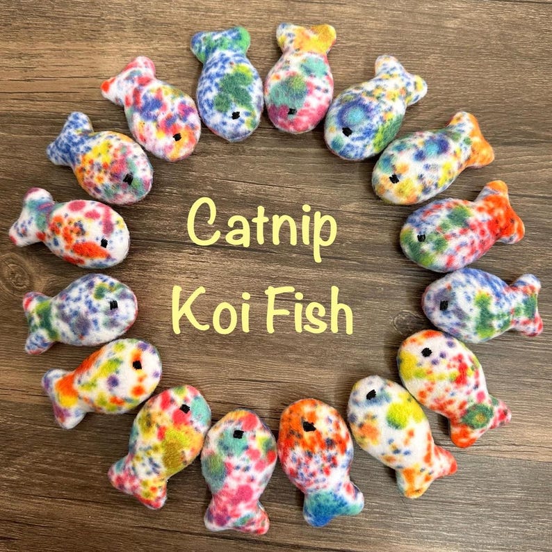 May include: A circle of 15 colorful catnip koi fish toys. The toys are made of soft, fuzzy fabric with a white base and colorful spots. The text "Catnip Koi Fish" is written in yellow letters in the center of the circle.