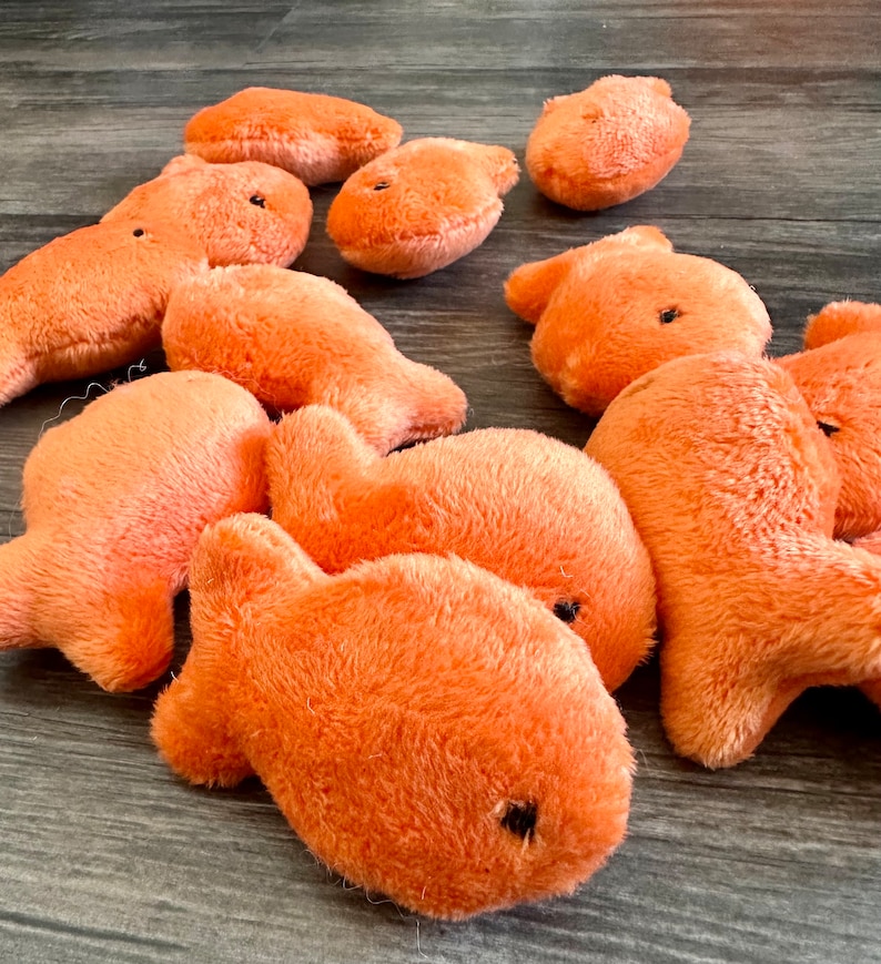 Pode incluir: Um grupo de dez brinquedos de peixe de pel&uacute;cia laranja. Os peixes s&atilde;o de diferentes tamanhos e formas, e t&ecirc;m olhos pretos.