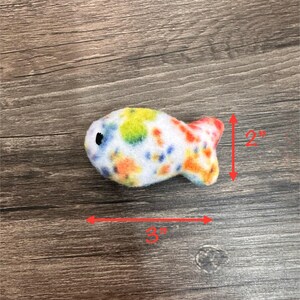 May include: A colorful, white, orange, yellow, and blue fish-shaped plush toy. The toy is 3 inches long and 2 inches tall.