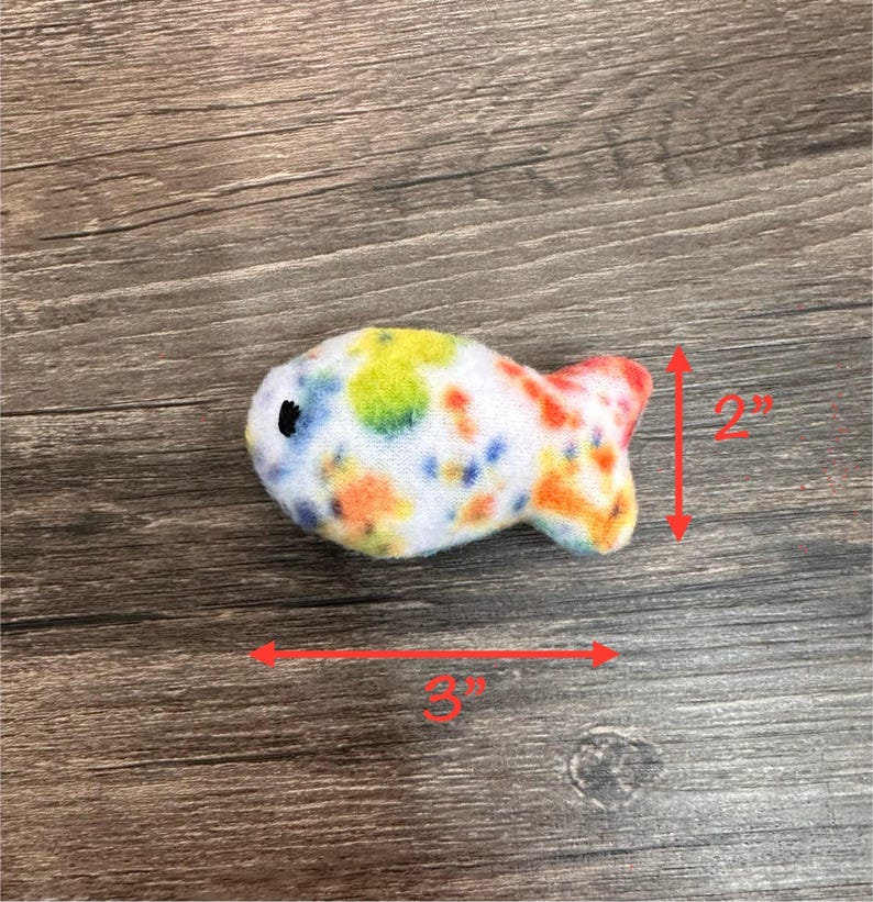 May include: A colorful, white, orange, yellow, and blue fish-shaped plush toy. The toy is 3 inches long and 2 inches tall.