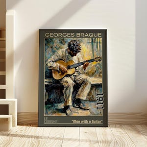 May include: A framed art print of Georges Braque's "Man with a Guitar" from 1911. The artwork shows a seated figure playing a guitar, in muted tones. The print is displayed on a wooden floor, leaning against a white wall.