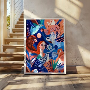 以下が含まれることがあります： 鳥、女性、花柄の鮮やかなイラストが描かれた額入りのアートプリント。青、オレンジ、赤のパレットを使用しています。プリントは木製の床に展示され、白い壁に立てかけられています。