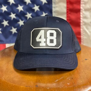 Pode incluir: Um chap&eacute;u de caminhoneiro azul marinho com um remendo preto e branco que diz "48".