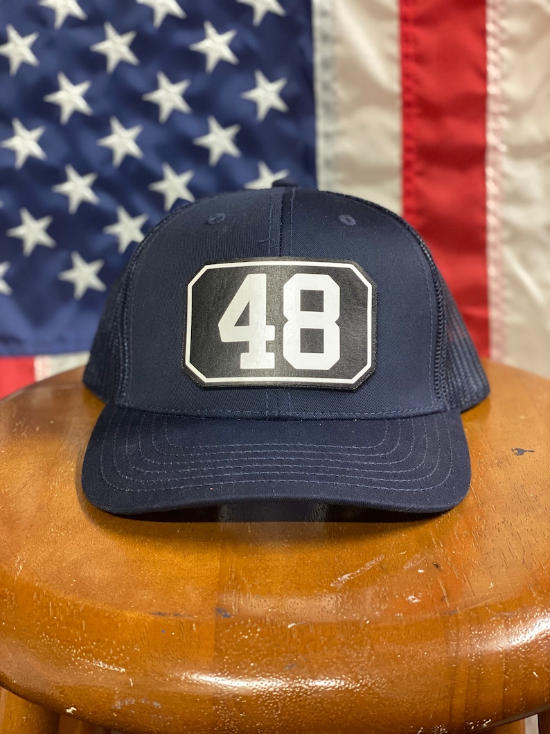 Pode incluir: Um chap&eacute;u de caminhoneiro azul marinho com um remendo preto e branco que diz "48".