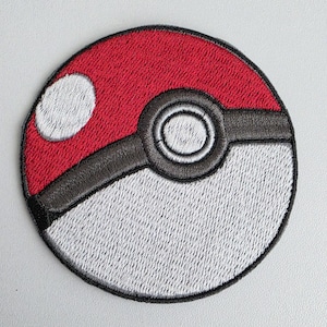 May include: A circular embroidered patch featuring a red upper half and a white lower half, separated by a black horizontal band. A central black circle with a white inner ring sits on the band, and a small white circle is on the red section.