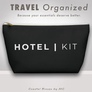 Könnte beinhalten: Schwarze Reisetasche mit dem Text "HOTEL | KIT" in Weiß. Die Tasche hat einen goldenen Reißverschluss und den Text "TRAVEL Organized" darüber. Der Text "Because your essentials deserve better" ist ebenfalls enthalten.
