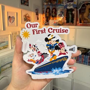 May include: A white sticker with a blue and yellow sun, the text "Our First Cruise", and a cartoon image of Mickey Mouse, Minnie Mouse, Pluto, and Goofy on a blue cruise ship. The text "Disney Cruise Line" is at the bottom of the sticker.