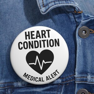 May include: A round white pin-back button featuring the black text HEART CONDITION at the top and MEDICAL ALERT at the bottom. In the center, a black heart icon contains a white EKG heartbeat line graphic, clearly indicating a medical status.