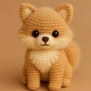 May include: A crocheted Shiba Inu dog figurine in shades of tan and cream. The handmade plushie has large black eyes, a fluffy chest, and a small, rounded tail. The dog is sitting on a solid tan background.