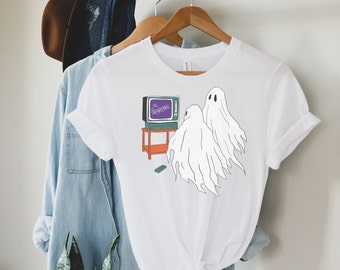 May include: White t-shirt with a graphic of two ghosts watching a television with the text "The Paranormal" on the screen.