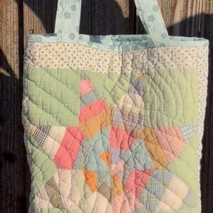 Peut inclure: Sac fourre-tout matelassé avec un motif d'éclat d'étoile. Le sac présente un patchwork de couleurs pastel, dont le rose, l'orange et le bleu, sur un fond vert. Les poignées et la bordure ont un motif floral. Le sac est en tissu.