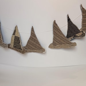 May include: A fabric bunting banner featuring triangular pennants in various shades of brown, beige, and dark gray. The pennants are crafted from different textile patterns, including small checks, plaids, and floral prints, all strung together.