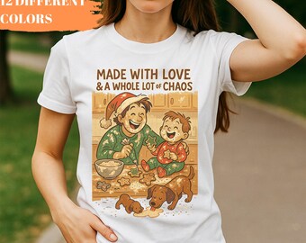 May include: White t-shirt featuring a colorful illustration of a parent and child baking cookies with two dogs. The text "MADE WITH LOVE & A WHOLE LOT OF CHAOS" is printed above the illustration. The words "12 DIFFERENT COLORS" are in the upper left corner.