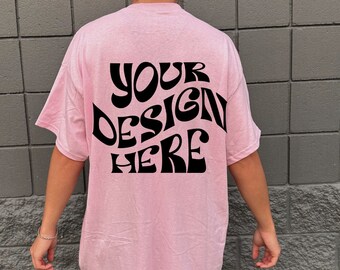 May include: A pink t-shirt with the text "YOUR DESIGN HERE" in black, retro-style lettering on the back.