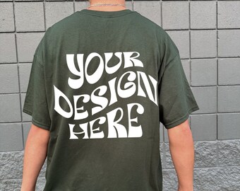 Può includere: Una maglietta verde scuro con una grafica bianca che dice "YOUR DESIGN HERE" in un font retrò.