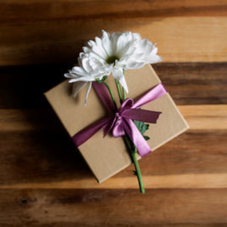 May include: A brown gift box tied with a pink ribbon and a single white daisy.