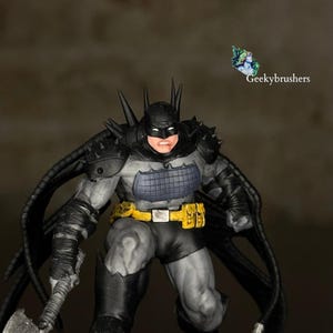 Puede incluir: Una detallada figura de Batman en pose de batalla. La figura es predominantemente gris y negra, con un cinturón utilitario amarillo y una placa pectoral azul. La figura tiene una capucha y una armadura de hombro con púas, y sostiene un arma. El texto "Geekybrushers" es visible.