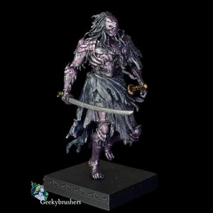 May include: A painted miniature figurine of a humanoid warrior with long hair, wearing tattered purple and dark metallic armor. The figure holds a curved silver sword in one hand and stands on a square black base. The text Geekybrushers is visible.