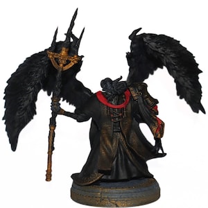 May include: A black and gold painted figurine of a winged figure with a staff. The figure is wearing a black robe with a red sash. The wings are spread out and the figure is holding the staff in its right hand.