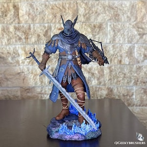 Puede incluir: Figura detallada de un caballero con armadura azul y marrón, sosteniendo una espada grande y una ballesta. El caballero tiene un casco con protuberancias en forma de alas y está sobre una base con detalles de llamas azules. Objeto de colección.