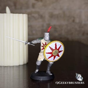 May include: A miniature knight figurine, wielding a silver sword and a shield with a red sun design. The knight wears a silver helmet, chainmail, and a cream-colored tunic. A red plume adorns the helmet. The figurine stands on a black base.