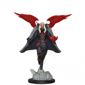 Puede incluir: Una figura miniatura de una figura alada con cabello blanco, que lleva una capa azul oscuro y sostiene una espada. La figura tiene alas rojas y está de pie sobre una base gris y blanca.