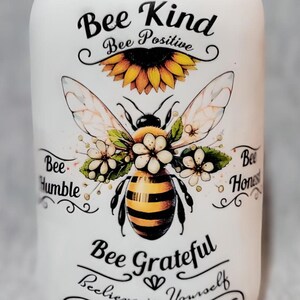May include: White ceramic jar with a bee and sunflower design. The jar has the text "Bee Kind", "Bee Positive", "Bee Humble", "Bee Honest", "Bee Grateful", and "Believe in Yourself".