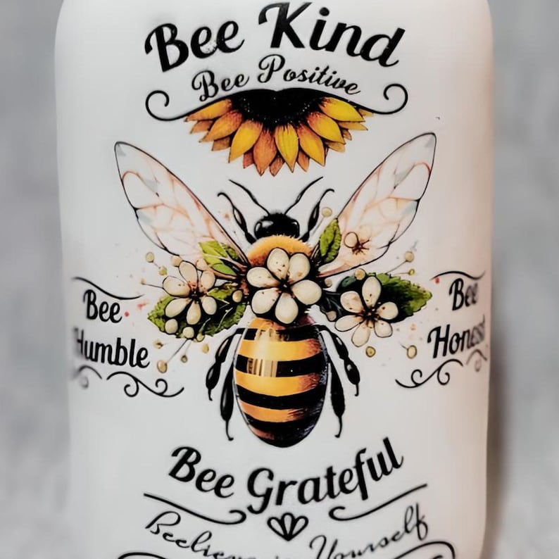 May include: White ceramic jar with a bee and sunflower design. The jar has the text "Bee Kind", "Bee Positive", "Bee Humble", "Bee Honest", "Bee Grateful", and "Believe in Yourself".