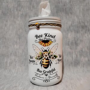 May include: White mason jar tissue dispenser with a bee and sunflower design. The jar has the text "Bee Kind, Bee Positive, Bee Grateful, Believe in Yourself".