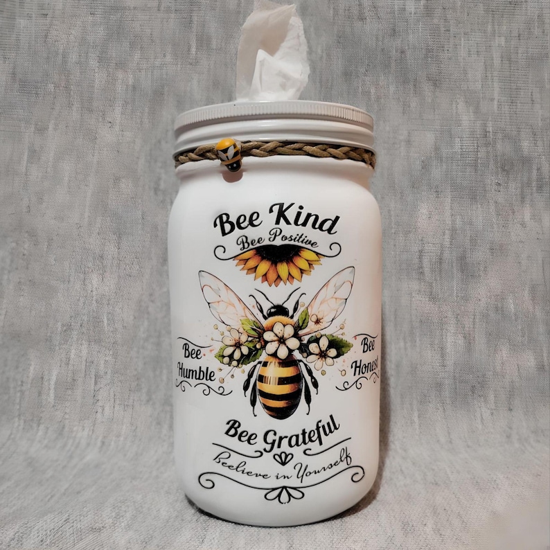 May include: White mason jar tissue dispenser with a bee and sunflower design. The jar has the text "Bee Kind, Bee Positive, Bee Grateful, Believe in Yourself".
