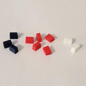 May include: An assortment of small, rectangular objects in red, white, and navy blue. The objects are evenly spaced and appear to be made of a solid material. The objects are arranged on a white surface.